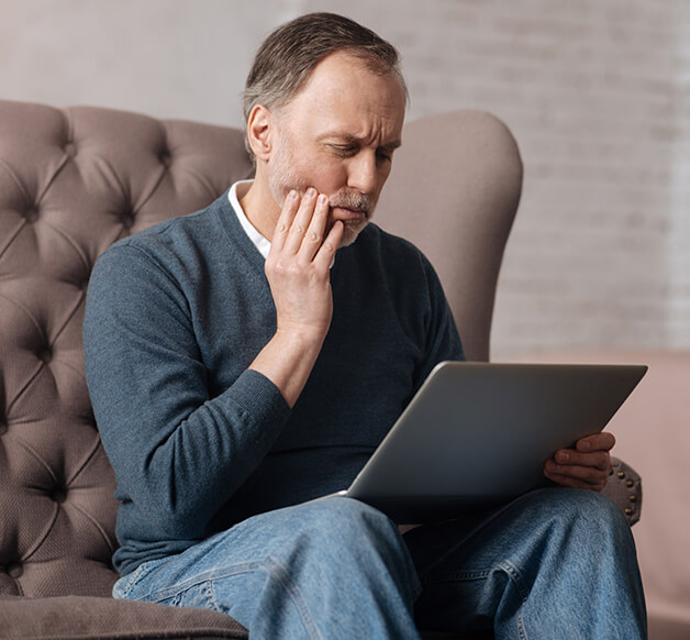 man holding his jaw in pain while looking at his laptop